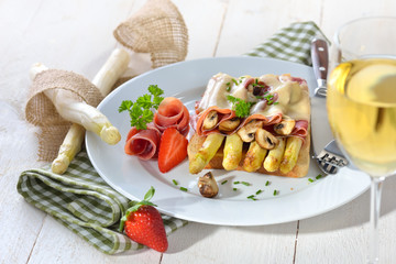 Überbackener Toast mit gebratenem weißen Spargel, Serrano-Schinken, Champignons und einer Scheibe Schnittkäse, dazu ein Glas Weißwein -  Baked toast with fried asparagus, ham, mushrooms and cheese
