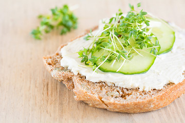 Eine Scheibe selbstgebackenenes Brot belegt mit Frischkäse, Gurke und Kresse