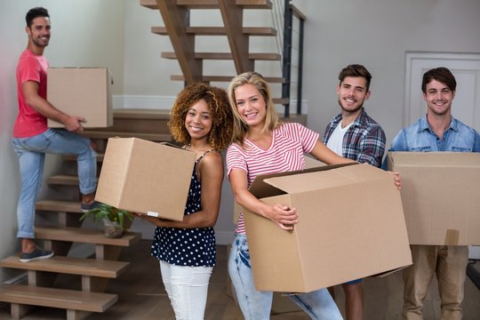 Cheerful young friends carrying carton in new house