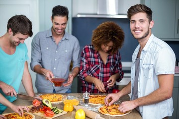 Obraz na płótnie Canvas Young man preparing pizza with friends on table