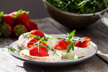 Multigrain rice cakes with strawberries fruit , soft mascarpone cheese and arugula for healthy breakfast.