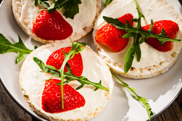 Multigrain rice cakes with strawberries fruit , soft mascarpone cheese and arugula for healthy breakfast.