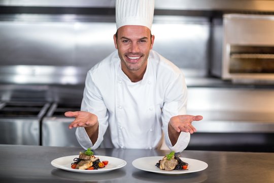 Portrait of smiling chef showing food plates in kitchen