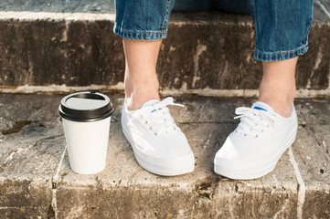 Close-up of woman wearing jeans and sneakers standing near coffe
