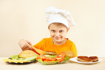 Young smiling boy in chef hat puts meat on the hamburger