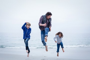 Cheerful family jumping at sea shore against clear sky - Powered by Adobe