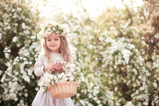 Smiling baby girl 3-4 year old holding basket with flowers outdoors. Childhood.