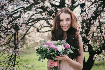 Woman in blooming trees. Woman with wedding bouquet in hands. Beautiful posing in a blooming apple garden.Spring mood. Young woman outdoors