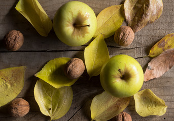 Two yellow apples, walnuts and autumn leaves on wood