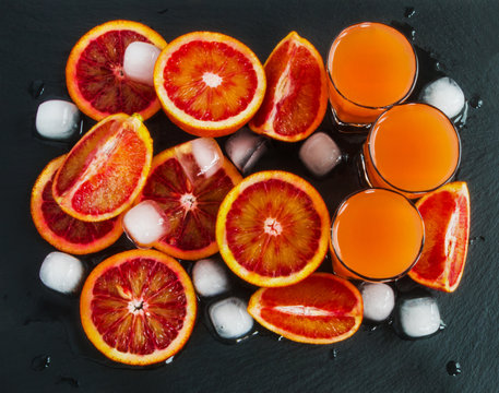Sliced Sicilian red oranges and orange juice in small glasses on black stone background. Top view.
