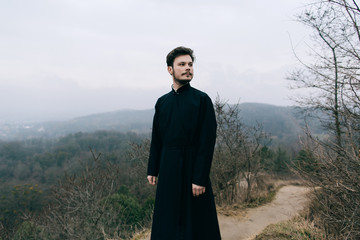 Portrait of handsome catholic bearded man priest or pastor posing outdoors in mountains