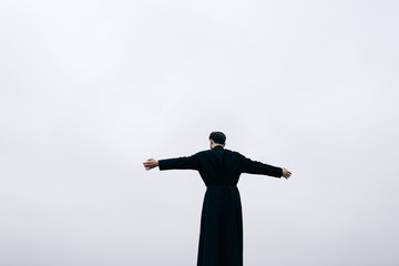 Priest bearded man raised his hands up on the hill above the town. Pastor posing outdoors in...