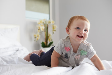 A happy baby girl crawling on a bed, copy space on left