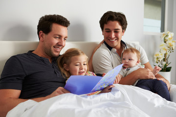 Fototapeta premium Male gay parents relaxing in bed with two kids