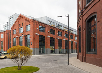 Extensive office complex exterior in loft style. Red brick buildings of former factory, gasholders. Evening architecture lighting, street lamps.