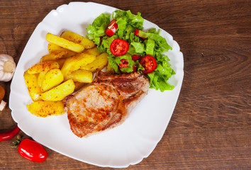 Juicy grilled meat fillet steak with fried potato and vegetables salad in a plate on wooden table