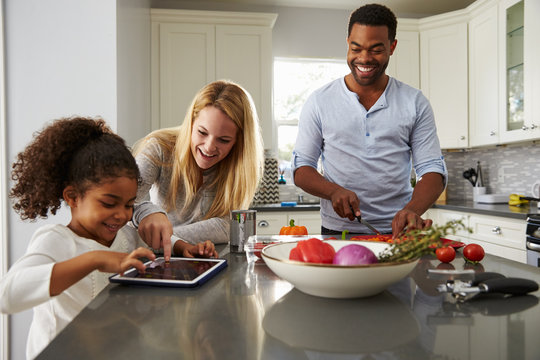 Mum and daughter use tablet computer, and dad prepares food