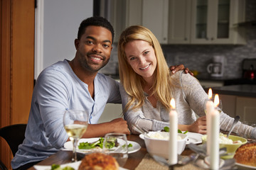 Romantic mixed race couple look to camera at meal in kitchen