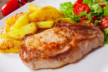 Juicy grilled meat fillet steak with fried potato and vegetables salad in a plate on wooden table