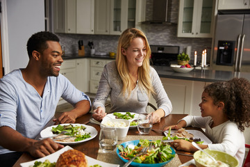 Girl and her mixed race parents dining in their kitchen
