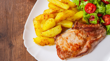 Juicy grilled meat fillet steak with fried potato and vegetables salad in a plate on wooden table