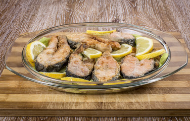 Fried fish ( with sliced lemon ) in a plate on wooden background
