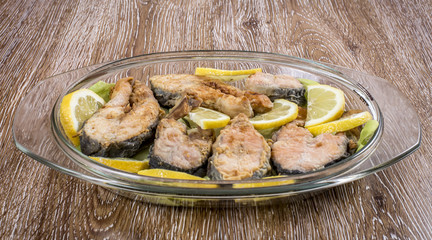Fried fish ( with sliced lemon ) in a plate on wooden background