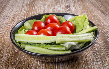 Tomato, cucumber and lettuce in a plate on wooden background