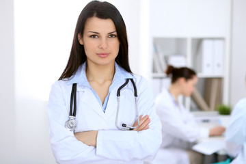 Fototapeta premium Brunette female doctor on the background of colleagues talking to each other in hospital
