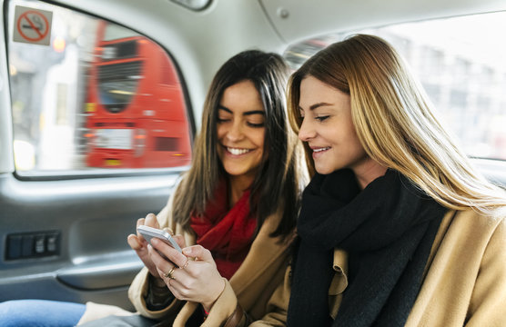 UK, London, Two young women using smart phone in black cab