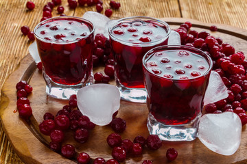 Cold cranberry drink in glasses, cranberries and pieces of ice on wooden background.