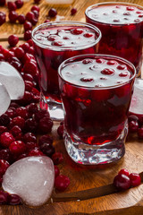 Cold cranberry drink in glasses, cranberries and pieces of ice on wooden background.