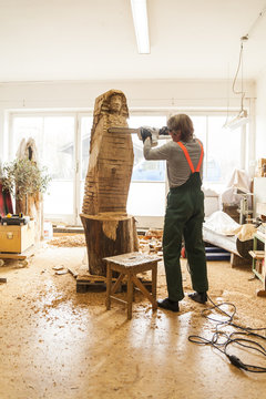 Wood carver in workshop working on sculpture with chainsaw