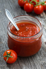 tomato sauce in a glass jar on a wooden background, vertical