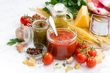 tomato sauce, pesto and ingredients for pasta on a white table