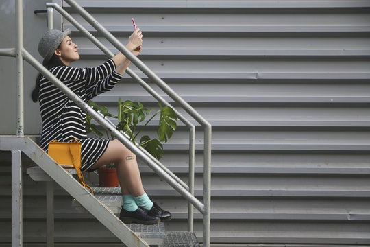 Young woman sitting on stairs taking a selfie with smartphone