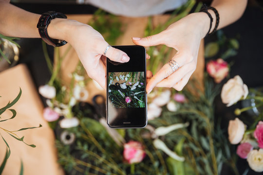 Woman florist taking pictures of flowers with mobile phone