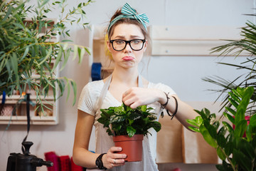 Sad woman florist holding green plant in flowerpot at shop