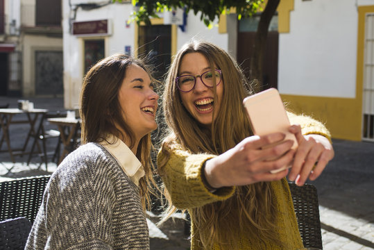 Laughing young woman taking a selfie with her friend at street cafe