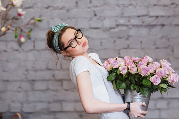 Cute tired young woman holding heavy bucket with pink roses © Drobot Dean