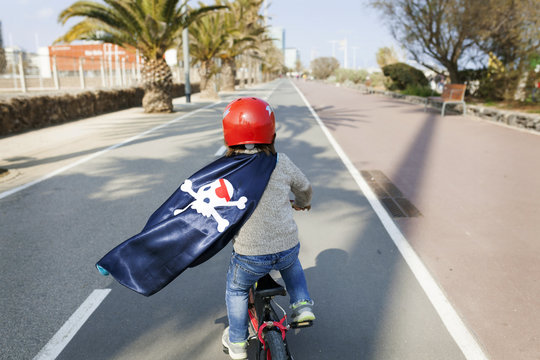 Spain, Barcelona, back view of little boy with a pirate cape riding bicycle on an empty street