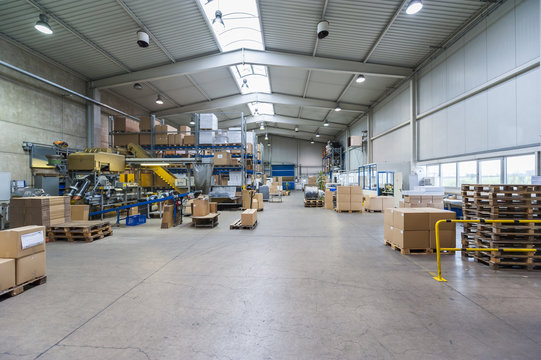 Empty industrial hall with stored packages, pallets and packaging machine