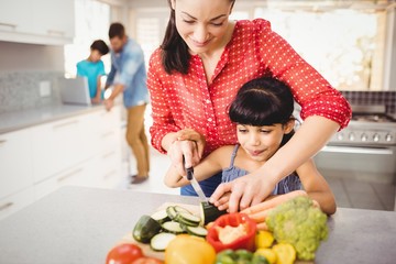 Happy mother teaching daughter to cut vegetables