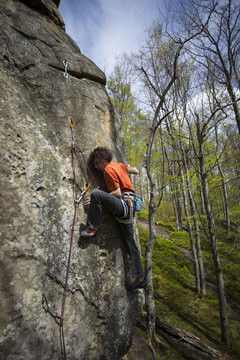 Athlete climbs on rock with rope.