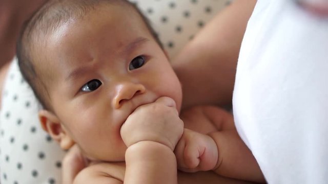 Hungry Asian baby sucking his fingers instead of mother breastfeeding