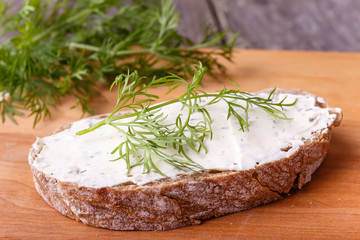 A slice of freshly baked ciabatta bread and healthy low fat cream cheese with dill and fresh green dill on wooden board.