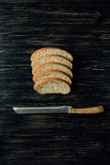 Sliced bread and knife on black wooden table