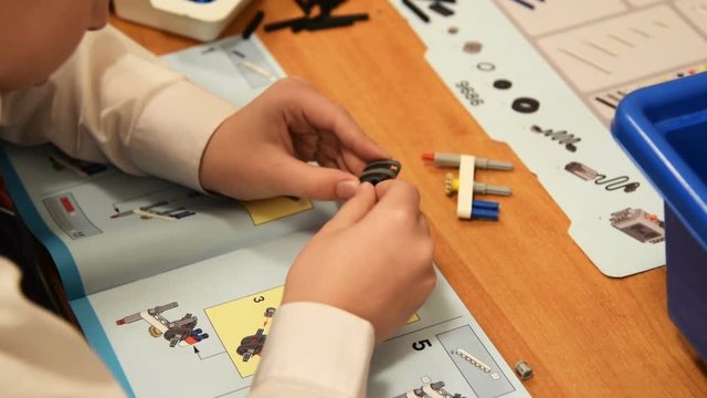 Pupil at the lesson of robotics at school. He following the instruction to make a robot from educational kit