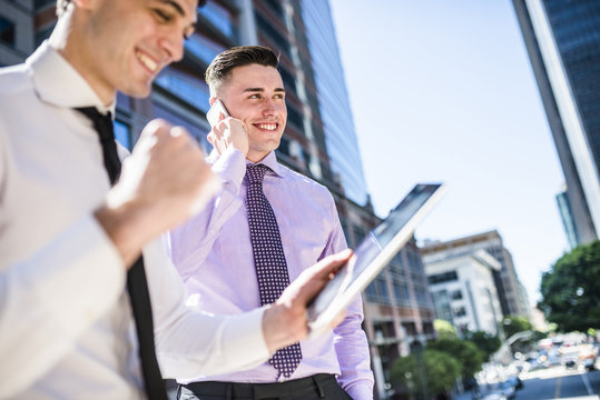 Two businessmen outdoors with tablet and cell phone