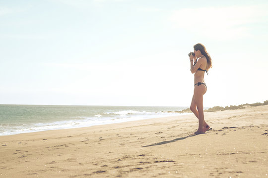 Spain, Tenerife, young woman standing on the beach taking a photo